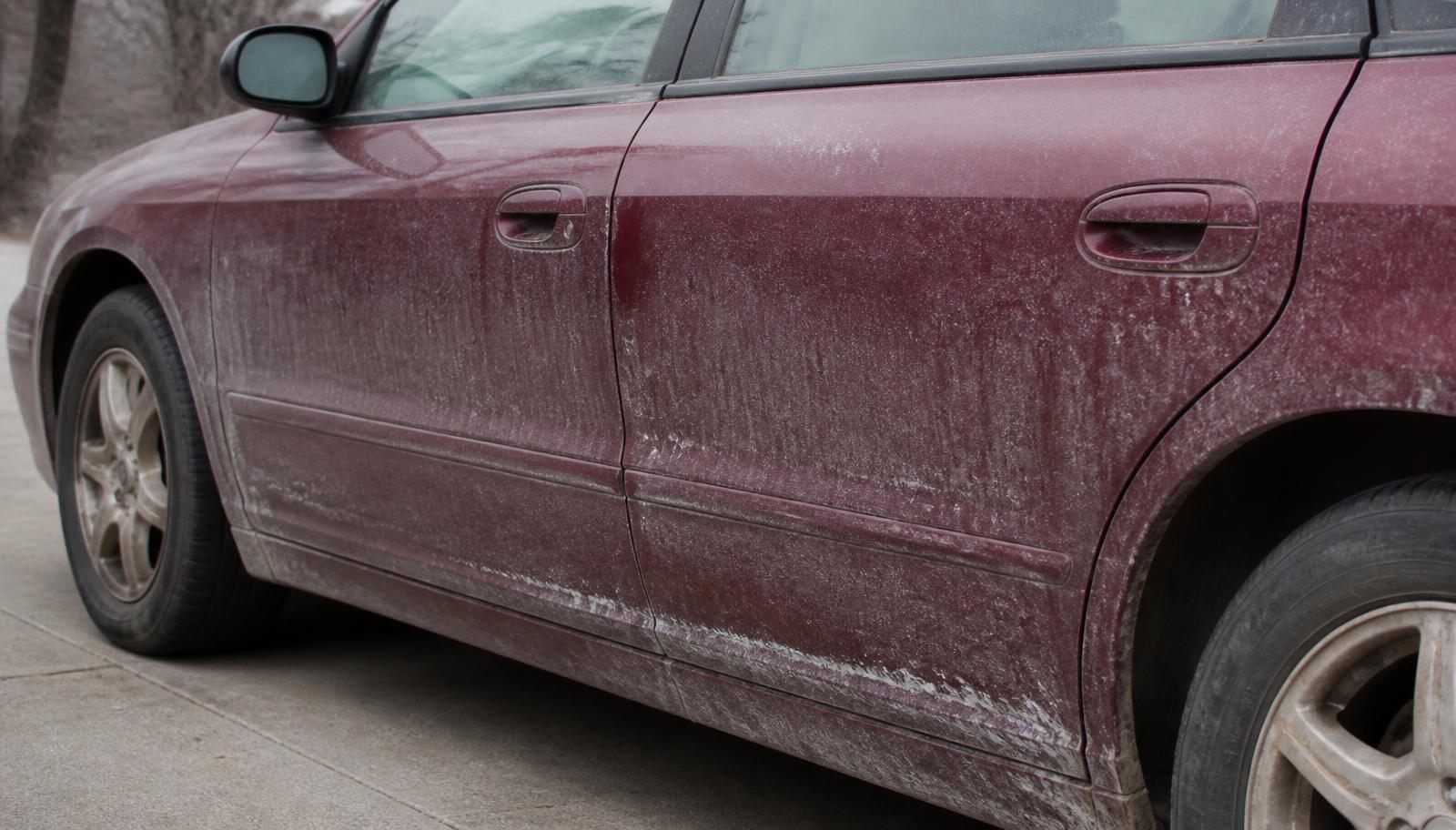 The side of a dark red car covered in road salt, dust and grime before cleaning.