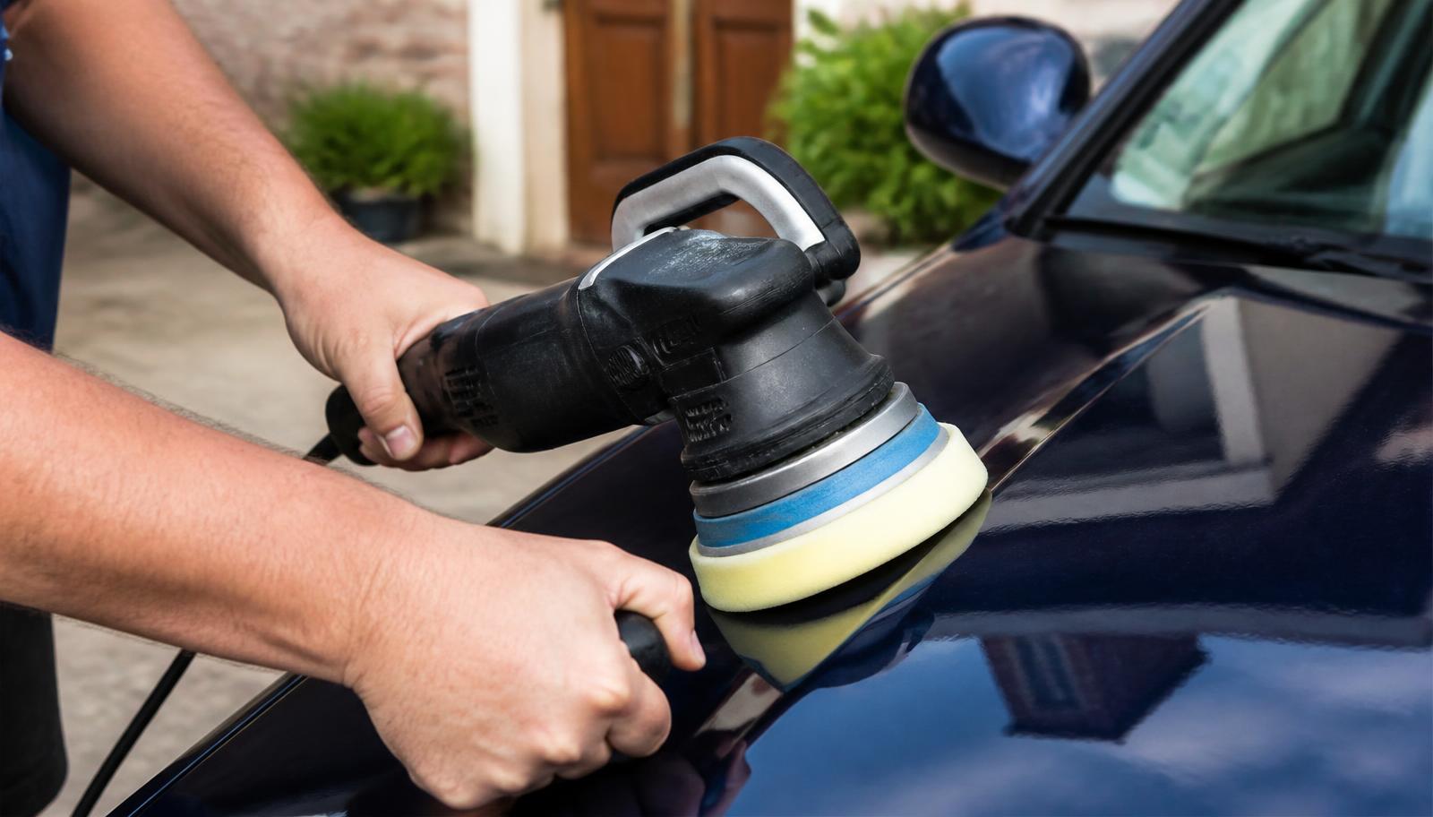 A machine polisher being used to buff the glossy dark blue bonnet of a car outdoors.