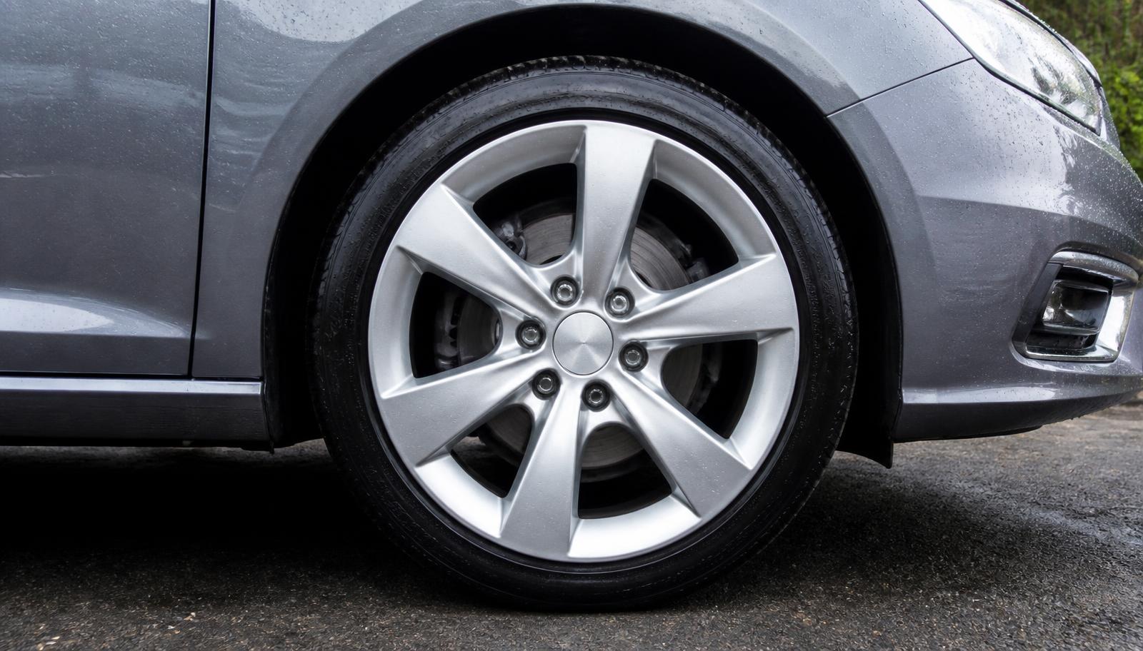 A close-up of a freshly cleaned alloy wheel face and tire on a grey sedan in a driveway.