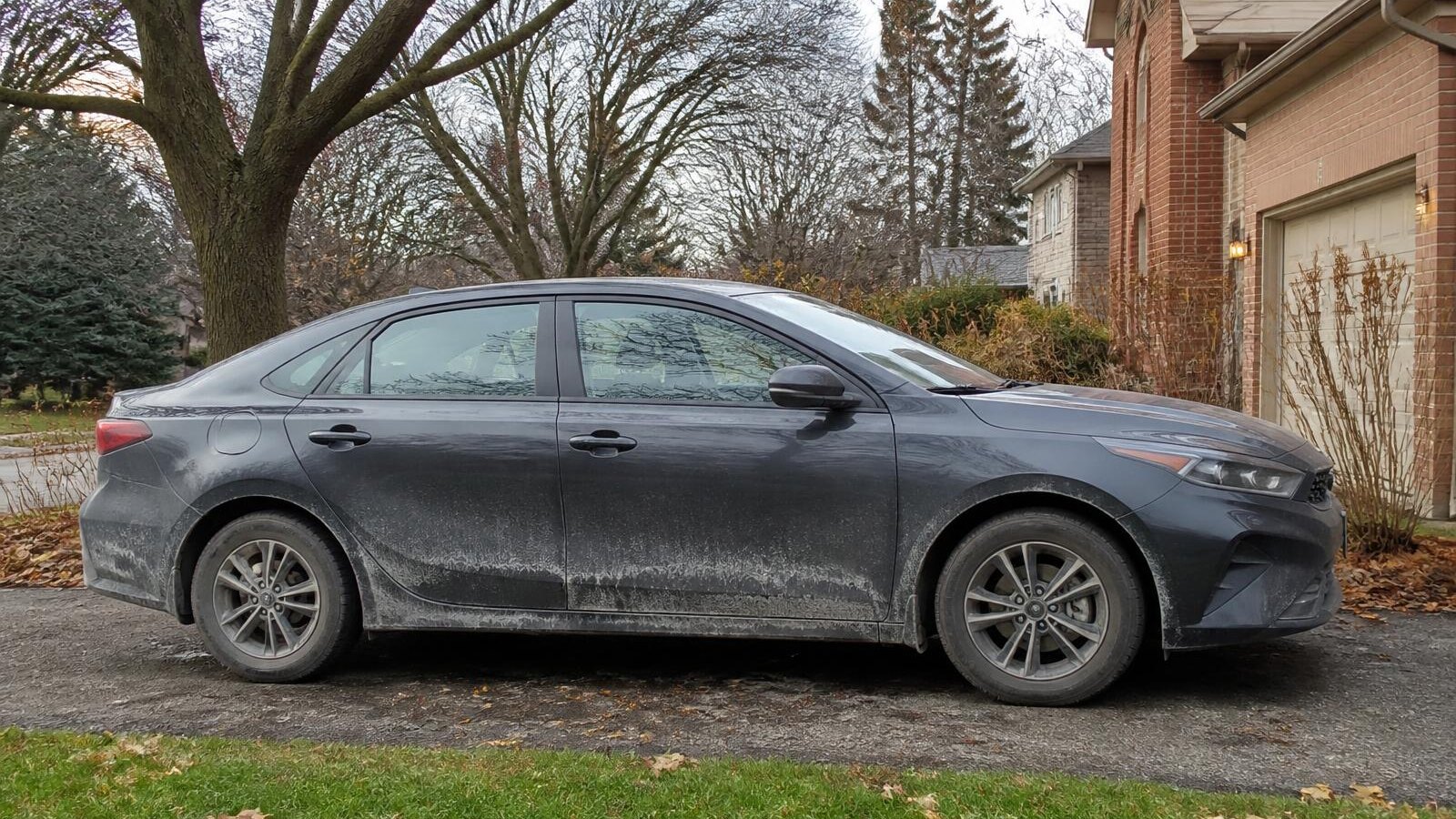 A dark grey sedan in an Ottawa driveway in late autumn with dried road salt and grime along the lower doors and wheels.