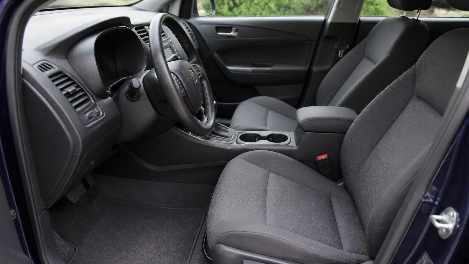 The clean interior of an ordinary family car: wiped dashboard, clean centre console and cup holders, and vacuumed grey cloth seats and mats.